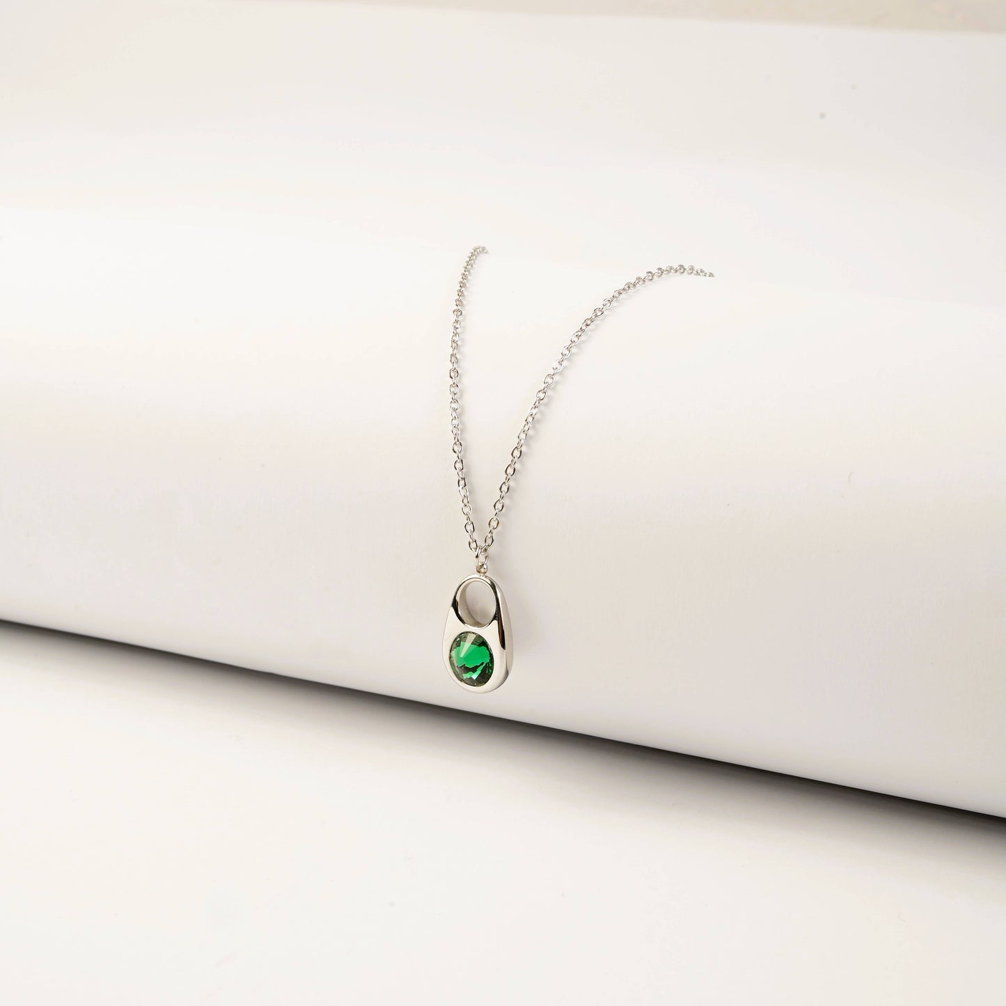 Silver necklace with a green gemstone pendant on a white surface