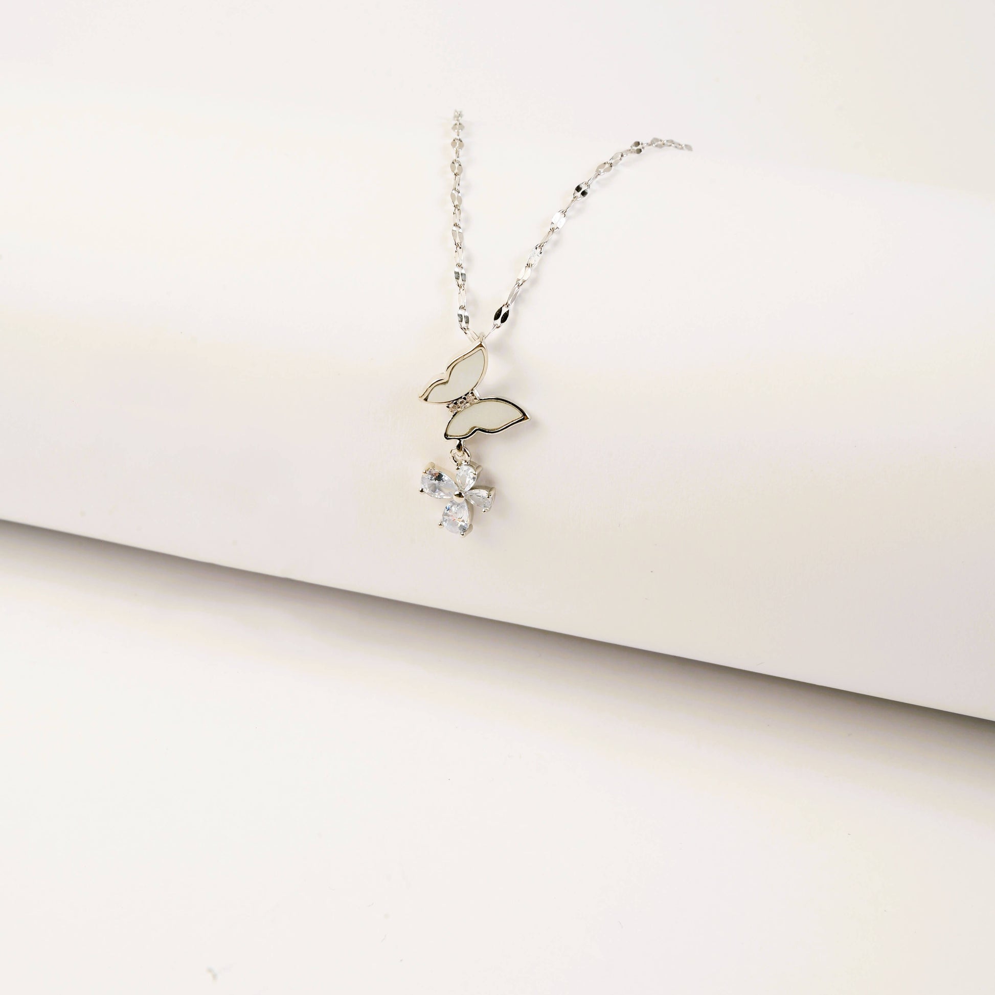 Delicate silver necklace with a small pendant on a light beige background